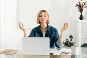 Relaxed young woman meditating at workplace after working day shift. Work life balance concept.