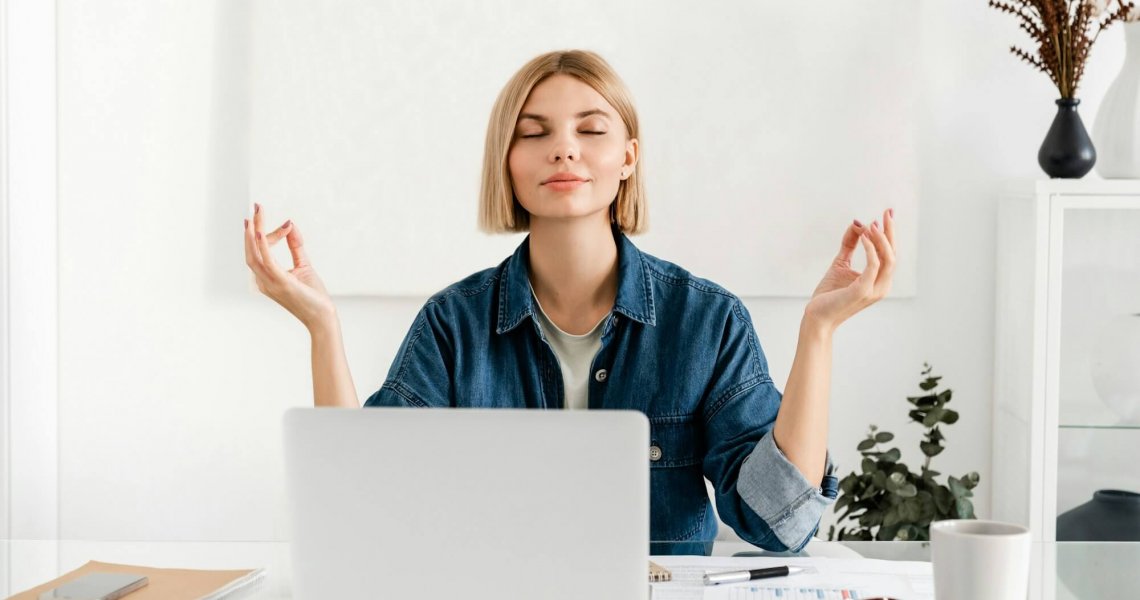 Relaxed young woman meditating at workplace after working day shift. Work life balance concept.